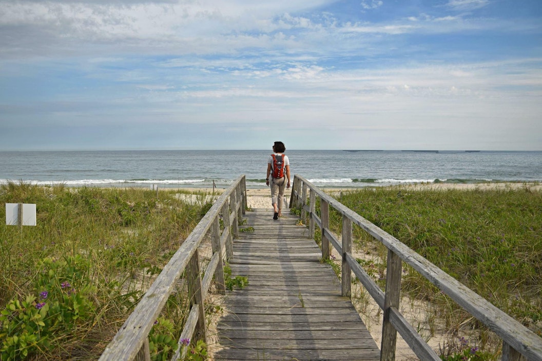 A person walks down to a beach on an elevated wooden boardwalk