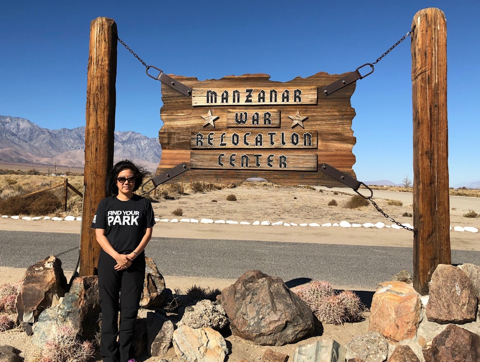 Kim stands next to a sign that reads "Manzanar War Relocation Center"