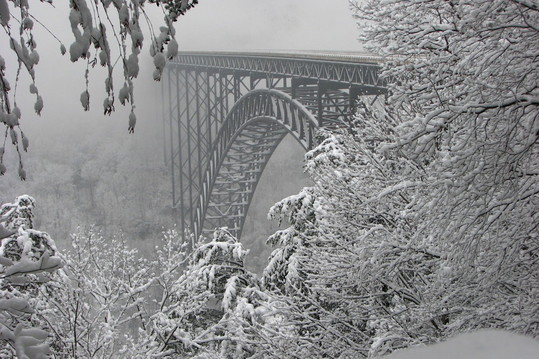 Snow covered steel bridge stretching between mountains