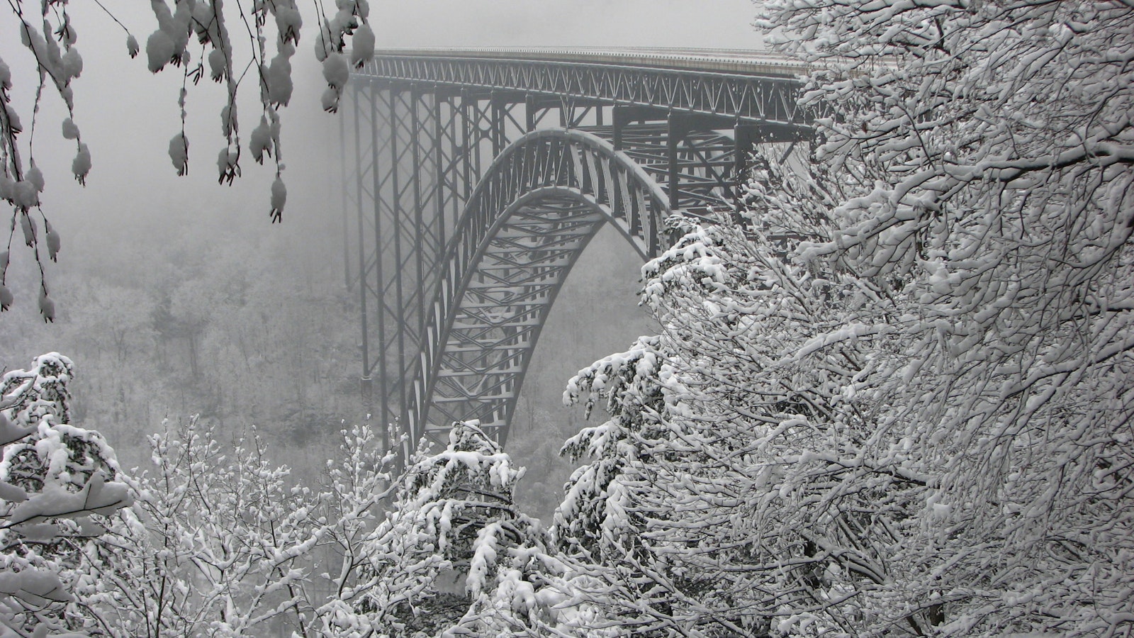 Snow covered steel bridge stretching between mountains