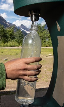 A hand reaches out to refill a waterbottle at a bottle refill station in a park