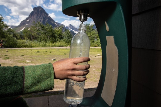 A hand reaches out to refill a waterbottle at a bottle refill station in a park
