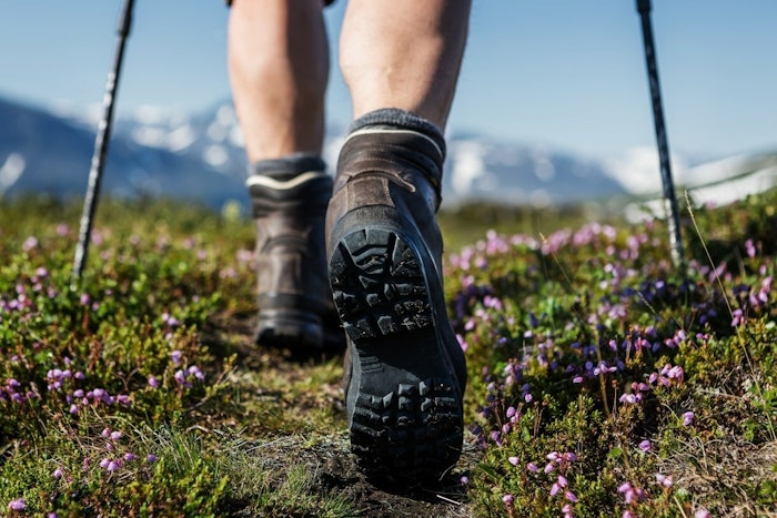 A close up photo of the bottom of a hiking boot and hiker's feet walking along a path