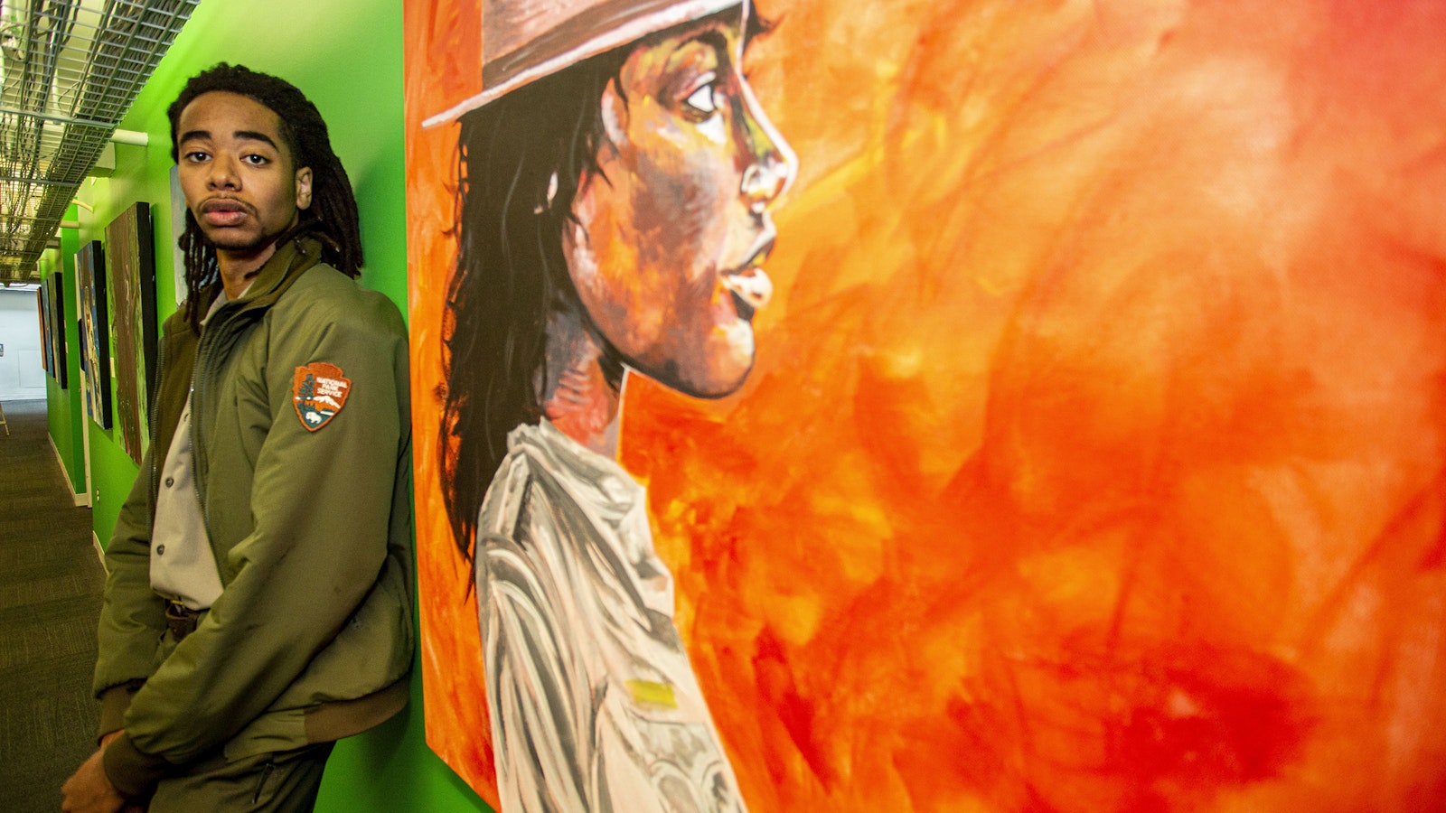 Elijah Prince stands in a hallway next to one of his paintings depicting a park ranger