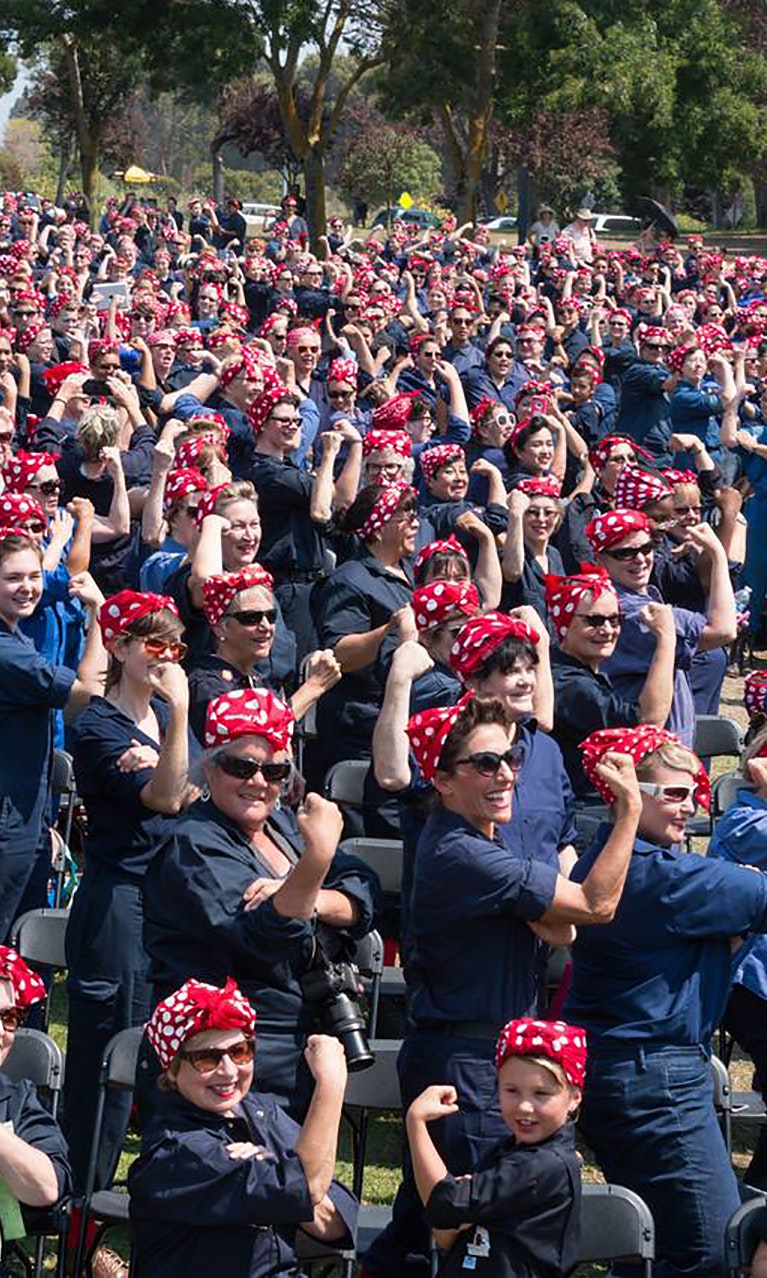 A crowd of people dressed as Rosie the Riveter pose for a photo