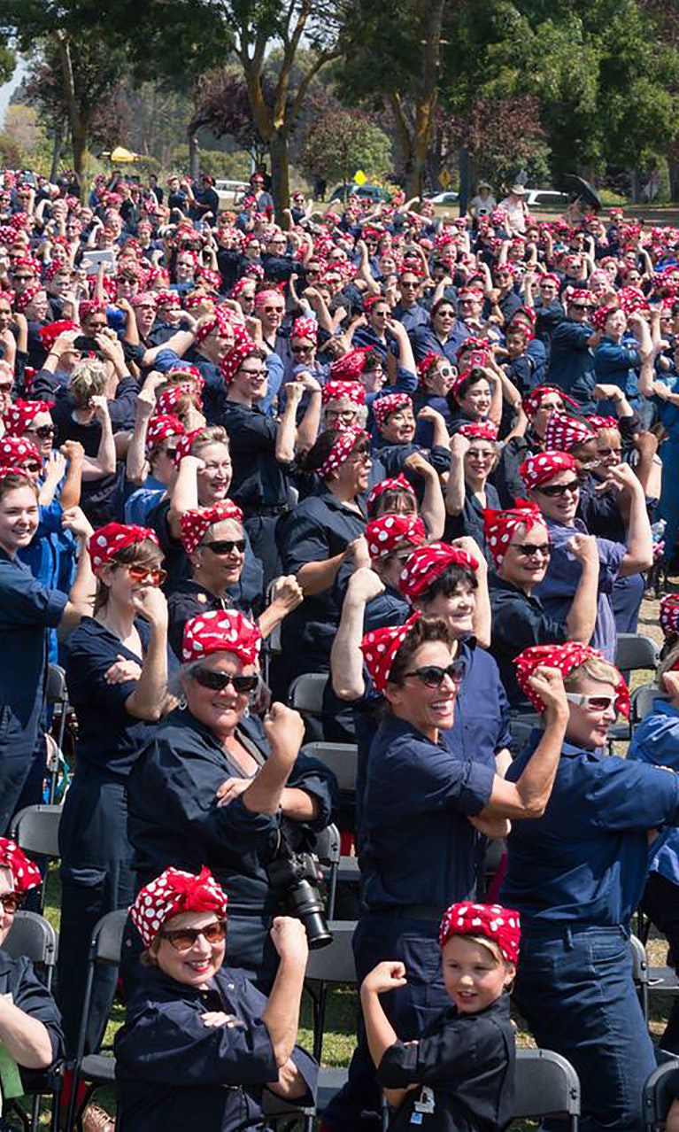 A crowd of people dressed as Rosie the Riveter pose for a photo