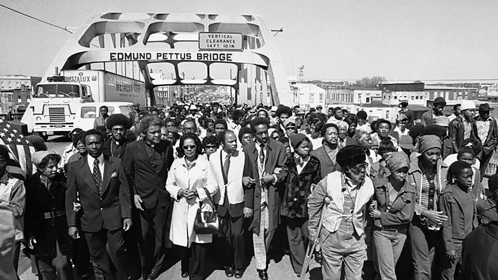 Black and white photo of a group of people marching across a bridge