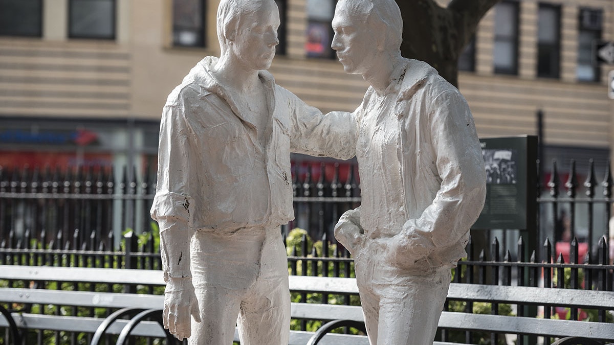 A statue of two men standing beside benches in a small park